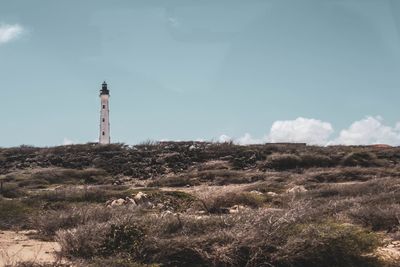 Lighthouse on field by building against sky