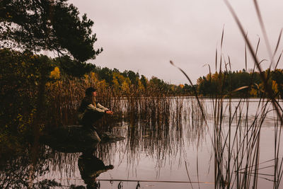 Man fishing in lake against sky