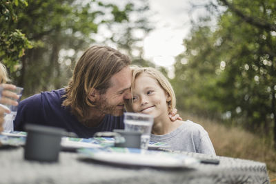 Affectionate father embracing daughter at table in campsite