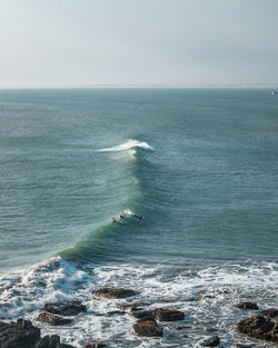 Scenic view of surfers in sea against sky