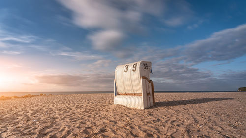 Hooded beach chair on sand against sky