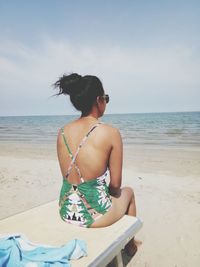 Rear view of woman looking at sea while sitting at beach