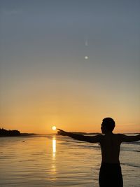 Silhouette man standing on sea against sky during sunset