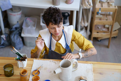 Woman artisian in pottery studio drawing on clay handmade teapot, female ceramist at work