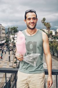Portrait of man holding cotton candy while leaning against railing 