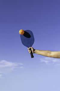 Low angle view of hand holding balloon against clear sky