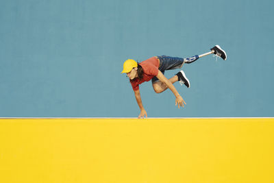 Low angle view of man jumping against yellow wall
