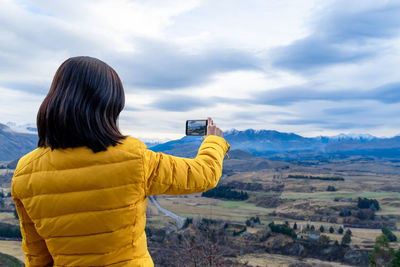 Rear view of woman photographing against sky
