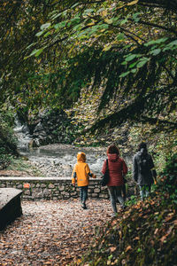 Rear view of women and child walking by the stream through a foliage covered path