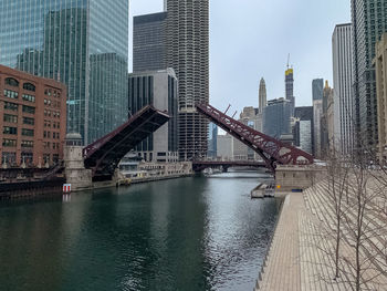 Bridge over river by buildings in city against sky