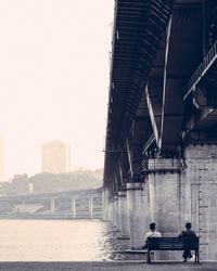 Rear view of men sitting on bench below bridge