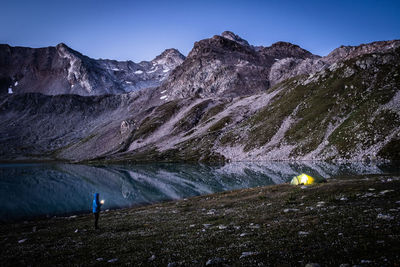 Man standing on land by lake against mountains and clear sky at night