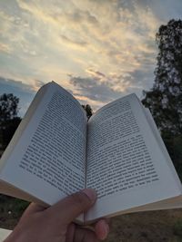 Midsection of person reading book against sky