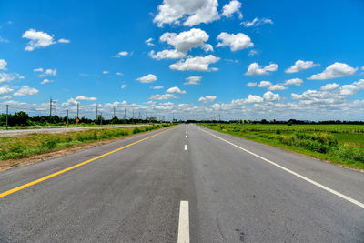 Empty road amidst field against sky