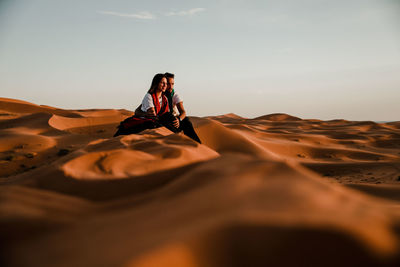 Woman on sand dune in desert against sky