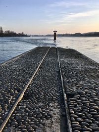 Railroad tracks by sea against sky during sunset