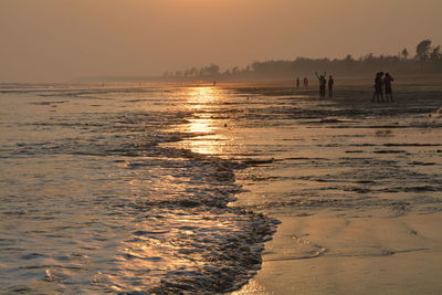 People at beach against sky during sunset