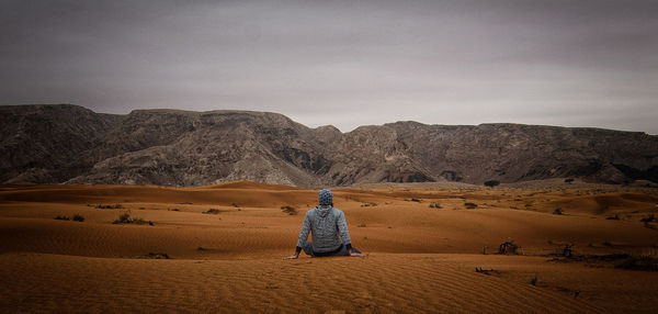Rear view of man relaxing at desert against sky