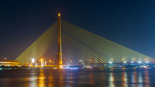 Illuminated bridge over river against sky at night