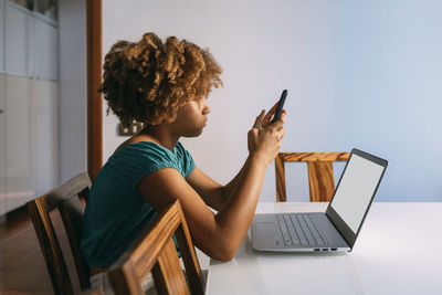 Girl sitting with laptop using smart phone at home