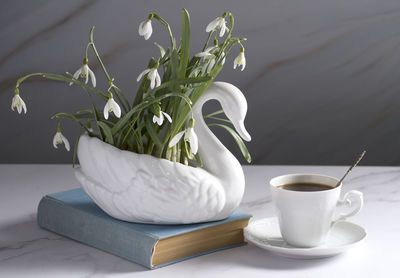 Still life with snowdrops in a ceramic vase like a swan, coffee in a white cup,  morning ritual