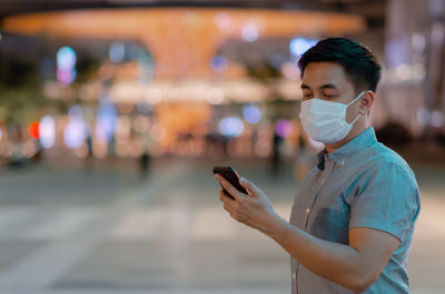 Asian man wearing face mask to protect from virus and looking at smartphone.