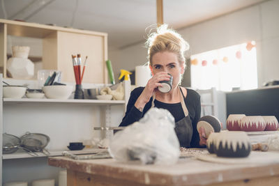 Portrait of woman having drink while sitting at table in workshop