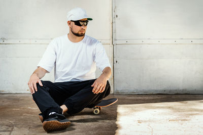 Young man looking away while sitting against wall