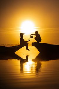 Silhouette people poured tea from teapot into cup against sun