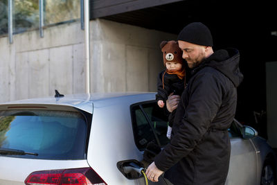 Man charging electric car while carrying baby