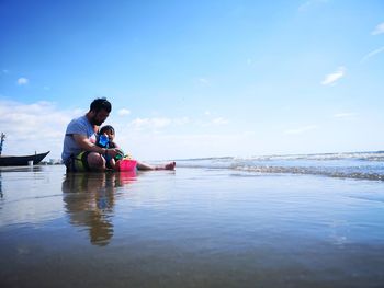 Father and daughter enjoying on shore at beach against sky