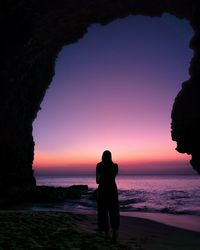 Silhouette woman standing at beach against sky during sunset