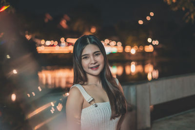 Portrait of smiling young woman standing in city at night