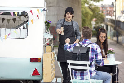 Salesman giving fork container to male customer outside food truck