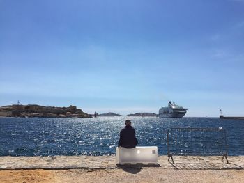 Rear view of man sitting at shore looking at view