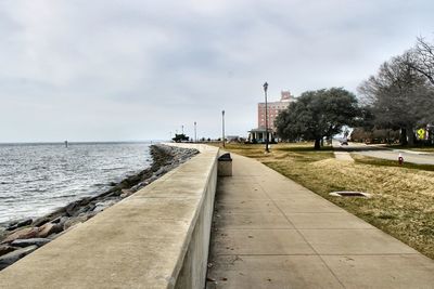 Scenic view of park next to sea against cloudy sky