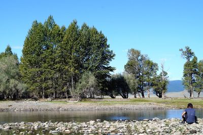 People sitting by lake against clear sky