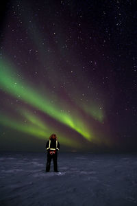 Full length of man standing on snow covered landscape against aurora borealis