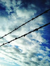 Barbed wire fence against cloudy sky