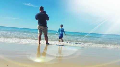 Rear view of father with daughter standing on beach against sky