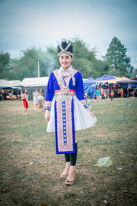 Portrait of smiling young woman in traditional clothing standing on grass against sky