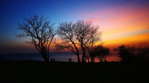 Silhouette trees by sea against romantic sky at sunset