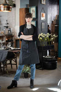 Full length portrait of confident young female owner standing with arms crossed at store