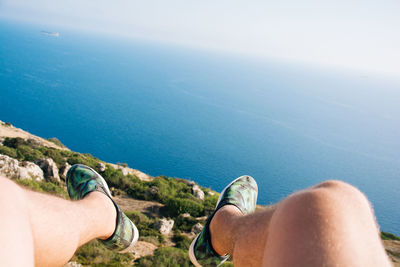 Low section of man dangling legs over sea