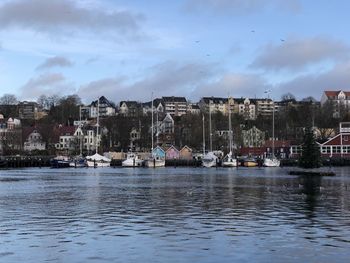 Sailboats in river by townscape against sky