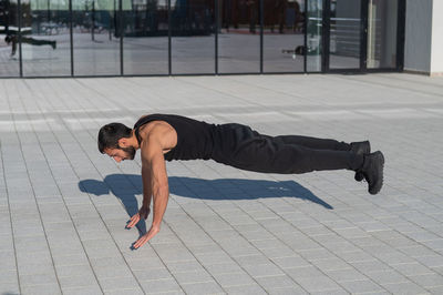 A man in black sportswear jumps while doing push-ups outdoors.