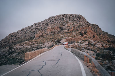 Rocky mountains with van moving on road against sky