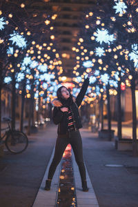 Woman standing on footpath against illuminated lights at night