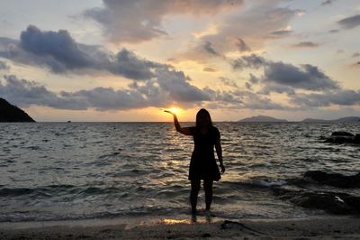 Silhouette woman standing on beach against sky during sunset