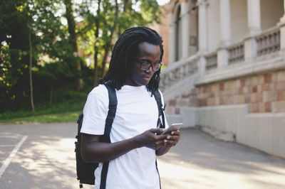 Young university student with backpack using mobile phone on road